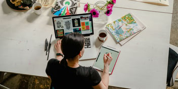 A woman sitting with a laptop and a tablet working on a design.