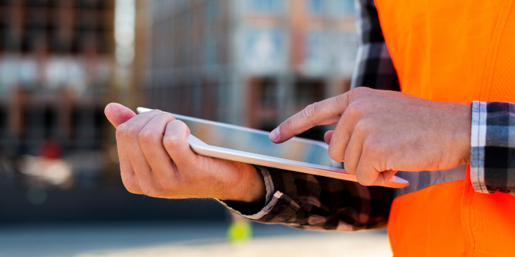 A man holding a tablet on a construction site.