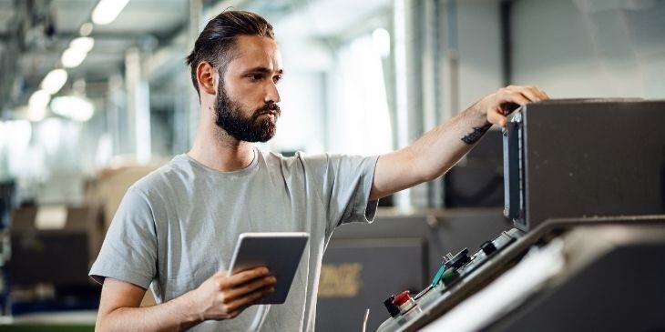 A man is holding a tablet and checking the machinery.