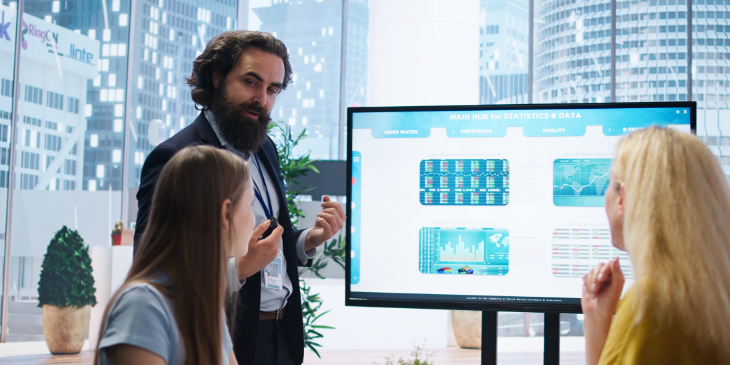 A man showing data on digital signage to his coworkers.